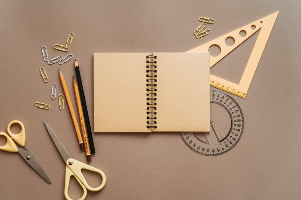 pexels photo 5088008 Flat lay of school supplies featuring a spiral notebook, scissors, and stationery on a brown background.